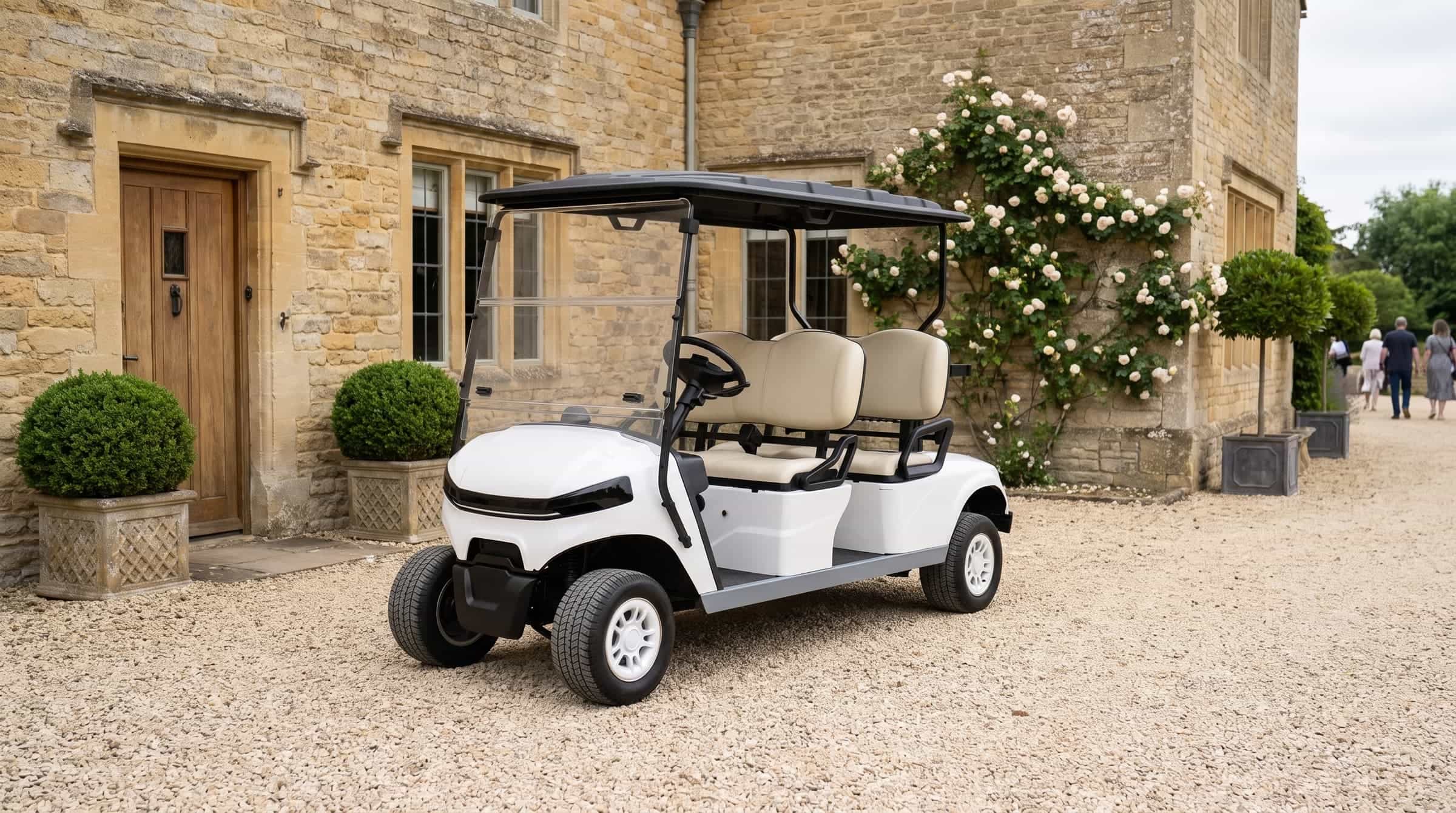 White four seater electric golf buggy with two forward facing benches on the gravel forecourt of a Cotswold stone country house
