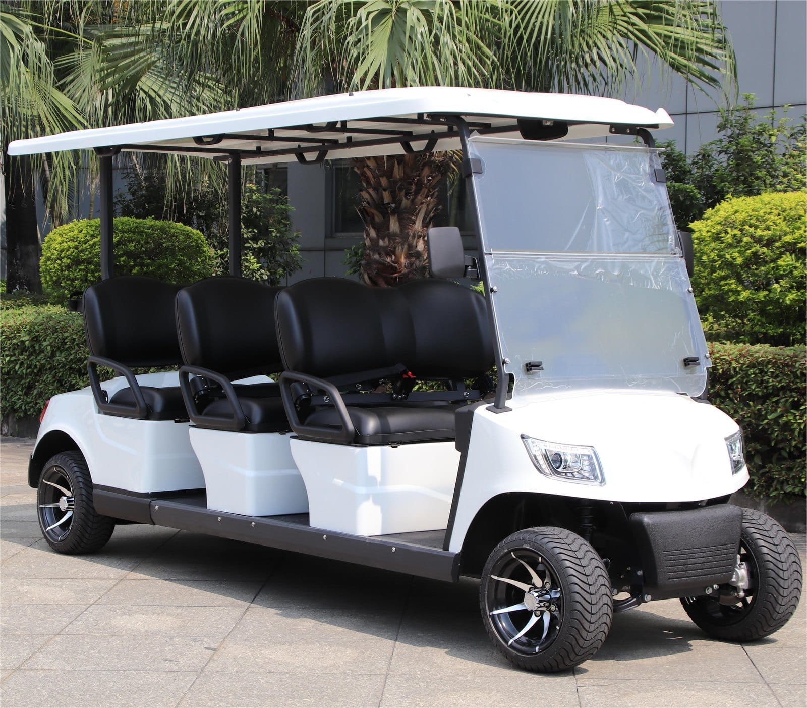White 6 seater electric golf buggy outdoors, showing the long canopy over three benches and black upholstery