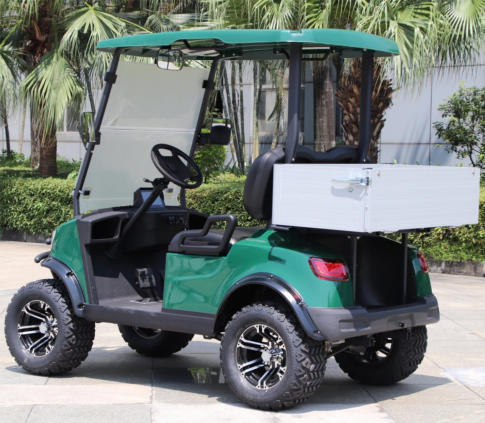 Dark green lifted 2 seater golf buggy outdoors, rear three quarter view with the drop side cargo bed lowered